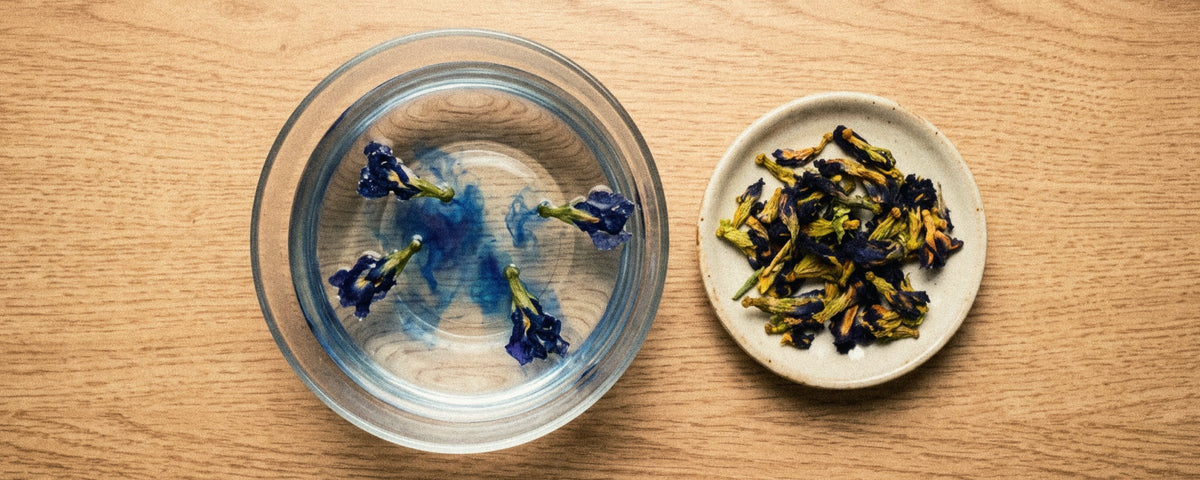 Анчан: синій настій із квіток Clitoria ternatea у скляній чашці, поруч сухі індигові квітки та скибочка лимона